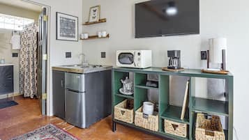 Cozinha compacta com geladeira, torradeira, cafeteira e TV de tela plana fixada na parede.