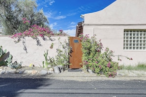 Ein Gebäude mit Stuckfassade, einem Holztor und rosa blühenden Pflanzen.