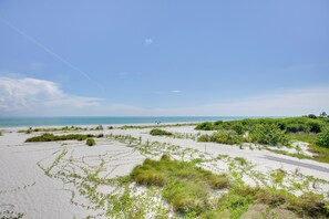 Ein Strand mit weißem Sand, grüner Vegetation und blauem Himmel.
