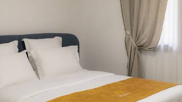 Ein Hotelzimmer mit Bett, weißer Bettwäsche, einer senfgelben Tagesdecke und einem Fenster mit Vorhängen.