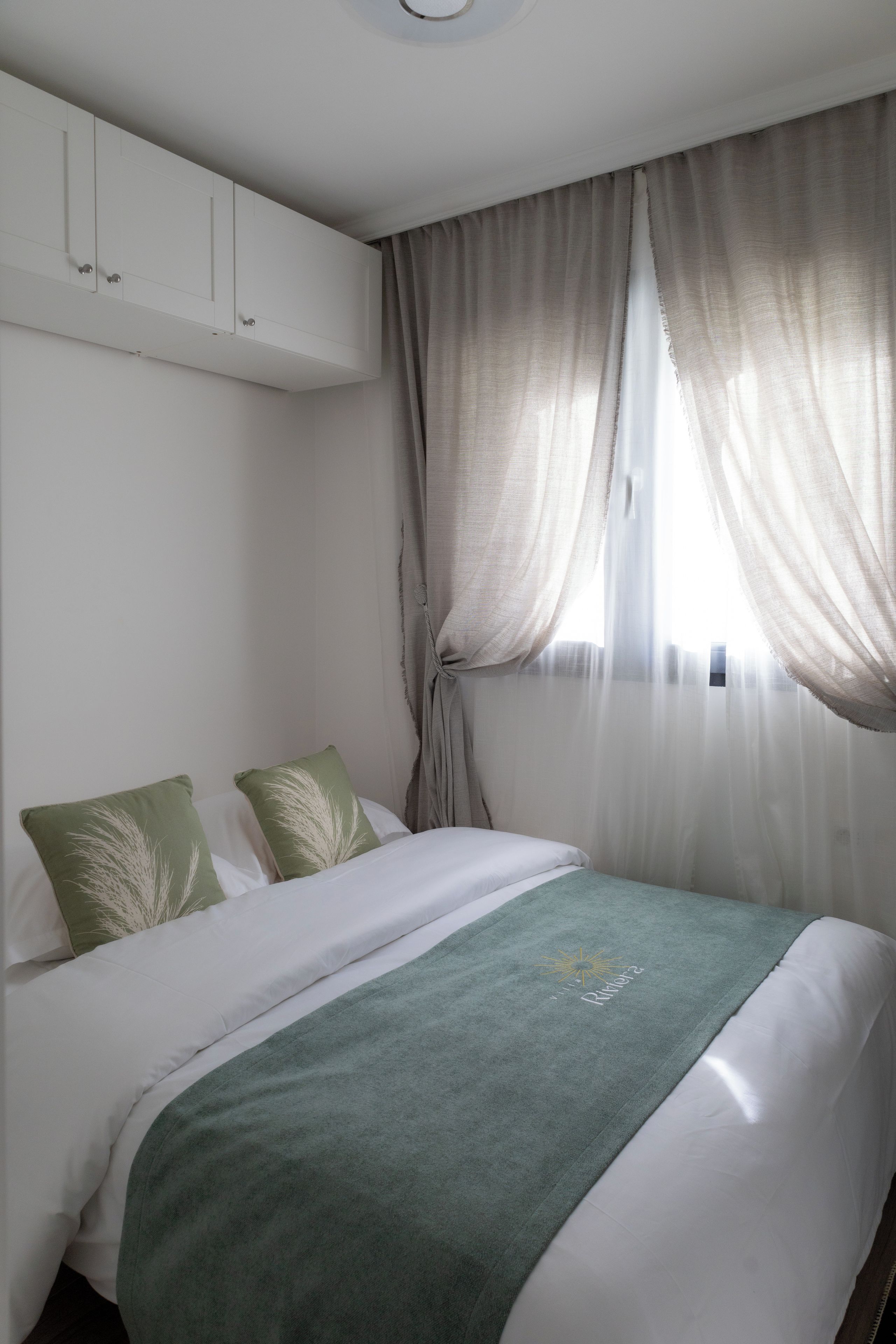 Une chambre d’hôtel avec un lit, une fenêtre avec des rideaux légers et un climatiseur fixé au mur.