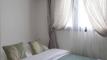 Een hotelkamer met een bed, een raam met dunne gordijnen en een wandairconditioner.