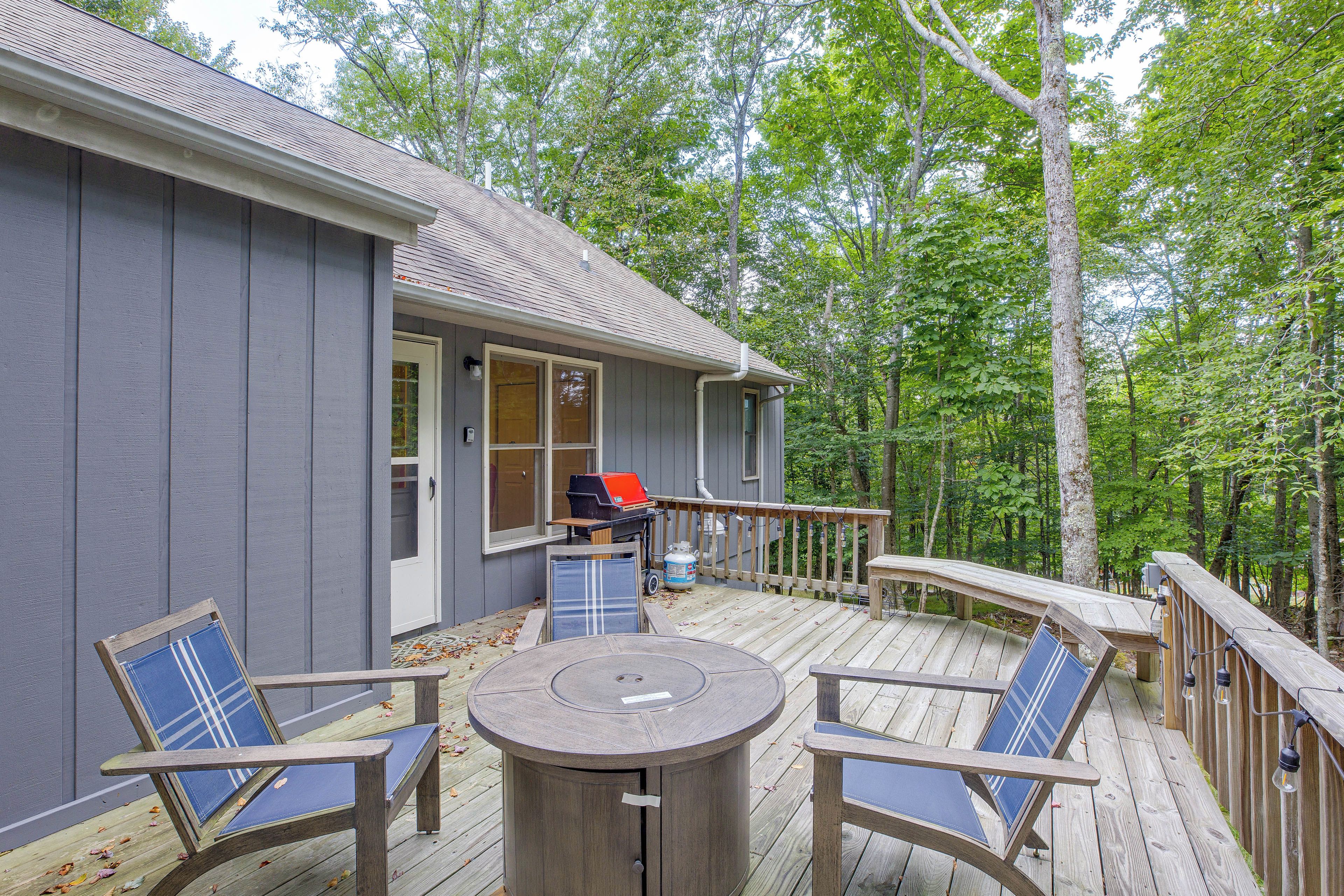 A deck with a round table and chairs, a barbecue grill, and a view of the forest.