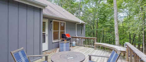 A deck with a round table and chairs, a barbecue grill, and a view of the forest.