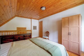 Ein Schlafzimmer mit Holzboden, einem Bett mit gesteppter Decke, einer hölzernen Kommode, einem Stuhl und einem Kleiderschrank.