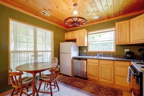 Una cocina con armarios de madera, un refrigerador blanco, un lavavajillas, una estufa y una mesa de comedor con sillas.