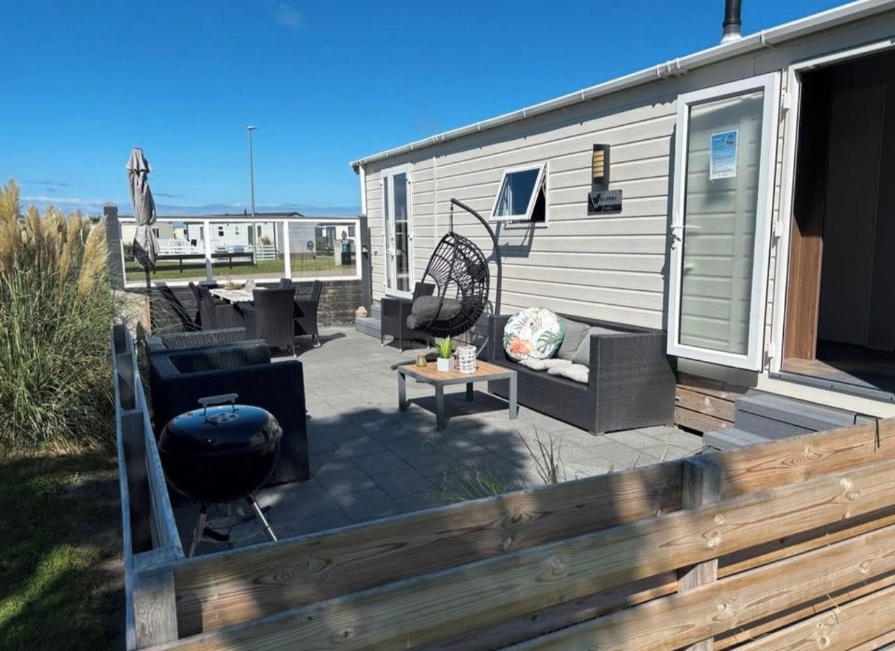 Un patio techado al aire libre con una parrilla, una zona de estar y vistas a una casa móvil.