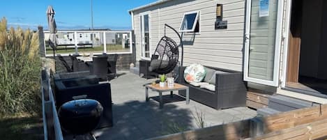 Eine überdachte Terrasse im Freien mit Grill, Sitzgelegenheit und Blick auf ein Wohnmobil.