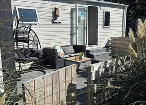 Ein Wohnhaus mit einer Terrasse, die Gartenmöbel, eine Holzterrasse und eine Schiebetür zu einer überdachten Veranda aufweist.