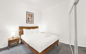 A neatly made bed in a hotel room with a wooden headboard, a bedside table with a lamp, and a framed picture on the wall. - The Chetwynd Elegant West Melbourne Hideaway (West Melbourne)