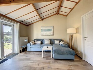 Ein Zimmer mit Holzboden, einem grauen Sofa mit gestreiften Kissen, einem weißen Beistelltisch, einer Stehlampe und einem Gemälde an der Wand.