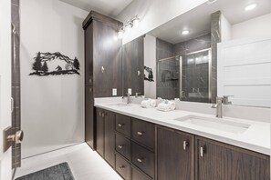 Une salle de bain moderne avec un meuble-lavabo à deux vasques, des meubles de rangement en bois foncé, un grand miroir et un espace douche.