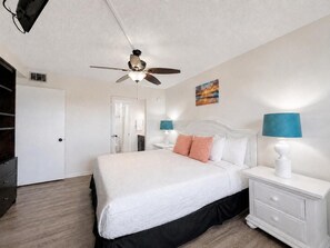 A hotel room with a bed, nightstands, a ceiling fan, and a painting on the wall. - The Summit 1028 (Panama City Beach)