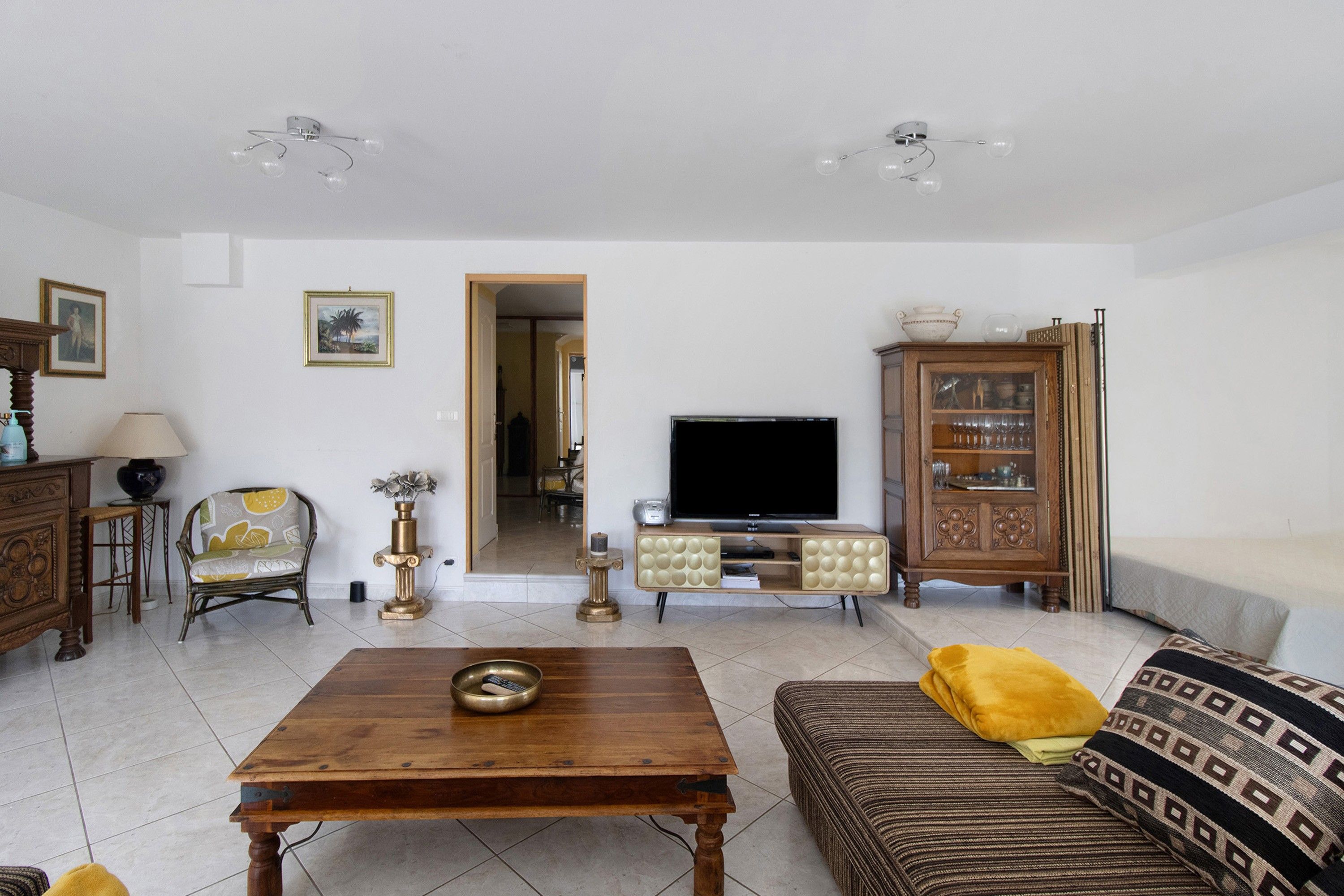 A living room with a wooden coffee table, a sofa with patterned cushions, a television, and a cabinet with glass doors.
