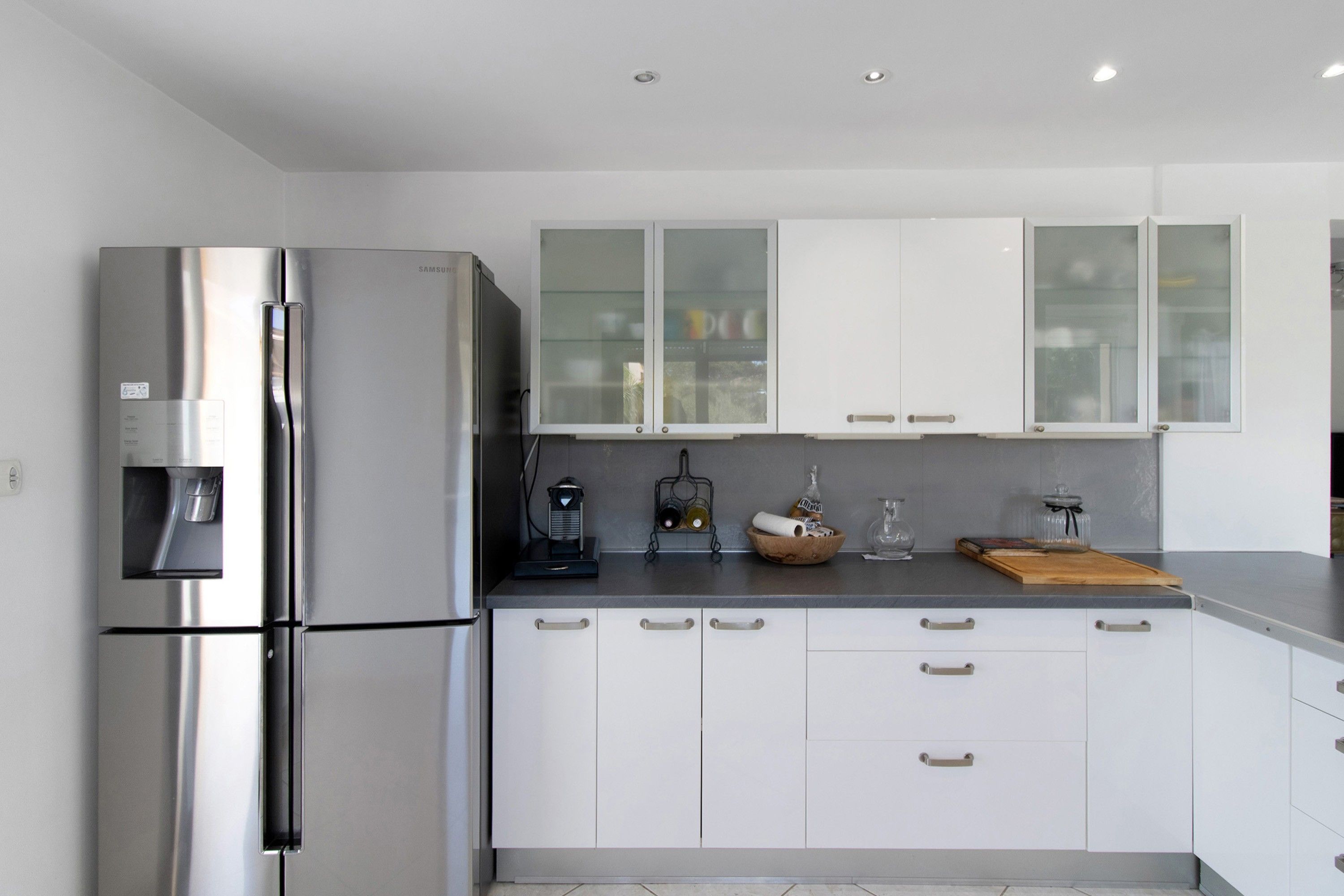 A modern kitchen with stainless steel appliances, white cabinetry, and a countertop with various items.
