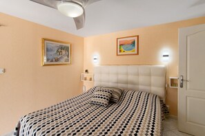A bedroom with a bed, a ceiling fan, wall-mounted lights, and two framed pictures.