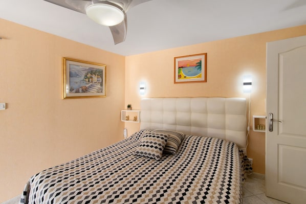 Une chambre à coucher avec un lit, un ventilateur de plafond, des lampes fixées au mur et deux tableaux encadrés.