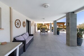 Eine überdachte Terrasse im Freien mit einer Couch, einem Tisch, Stühlen und dekorativen Wandbildern.