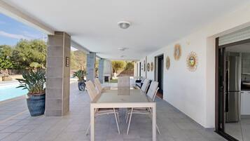 An outdoor patio with a dining table and chairs, a pool, and decorative wall art.