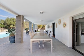 An outdoor patio with a dining table and chairs, a pool, and decorative wall art.