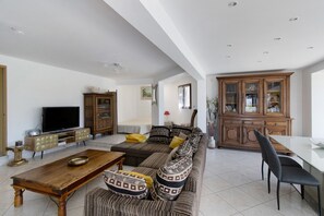 A spacious living room with a large sofa, a television, a wooden cabinet, and a dining area with a table and chairs. - Villa 'Portigliolo Michelangeli' with Sea View, Wi-Fi and Air Conditioning (Coti-Chiavari)