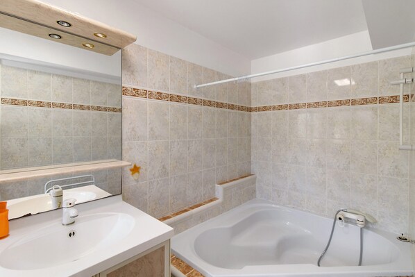 A bathroom with a bathtub, a sink, a mirror, and a shower area.