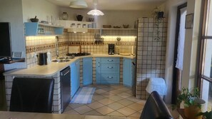 Une cuisine compacte avec des meubles bleus, une cuisinière à gaz, une machine à café et un dosseret carrelé.