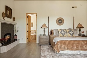A bedroom with a fireplace, a bed with patterned bedding, two bedside tables with lamps, and a decorative wall hanging. - Starry Night, Lake Views, Hot Tub, Mins 2 Lake (Big Bear Lake)