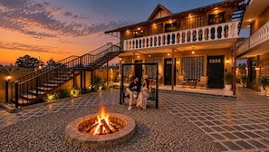 A two-story building with a fire pit in the center, outdoor seating, and a staircase leading to the upper level. - Luxuria Jim Corbett - By Moustache (Kaladhungi)