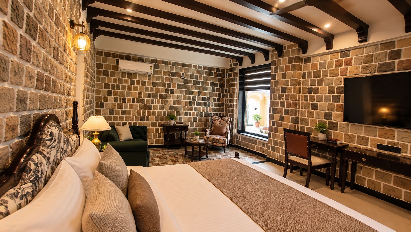 Quarto com parede de pedra, cama, televisão e janela.