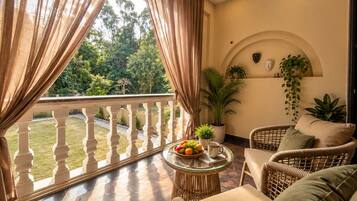 A balcony with a wicker chair, a small round table with fruit and a mug, and potted plants.