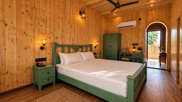 A wooden-paneled bedroom with a bed, nightstands, a desk, and an arched doorway leading outside.