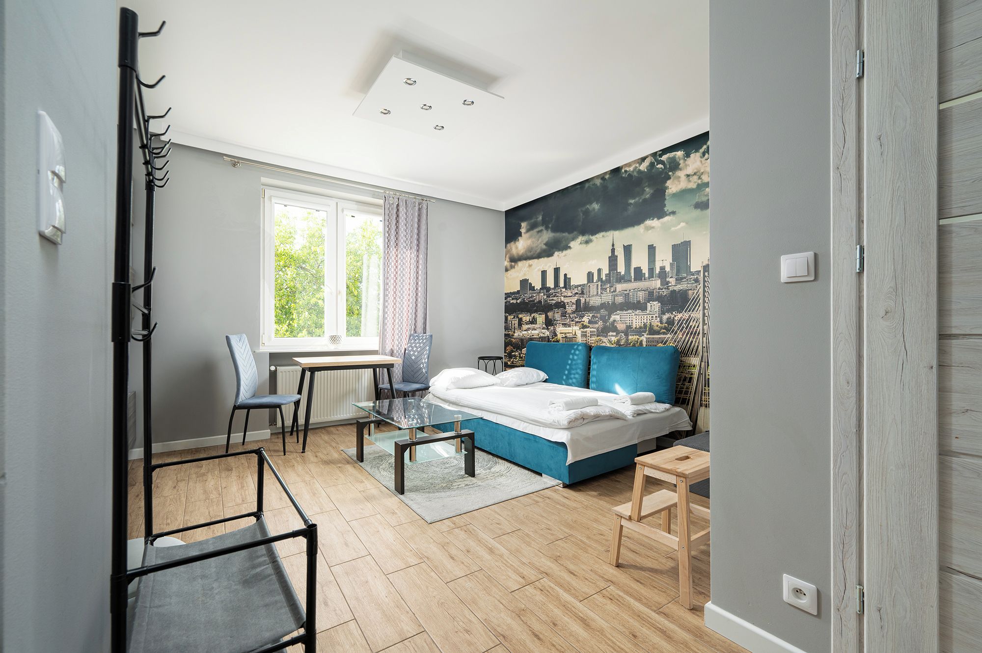 Ein modernes Schlafzimmer mit Stadtkulissen-Wandgemälde, einem Bett, einem Schreibtisch und einem Stuhl.
