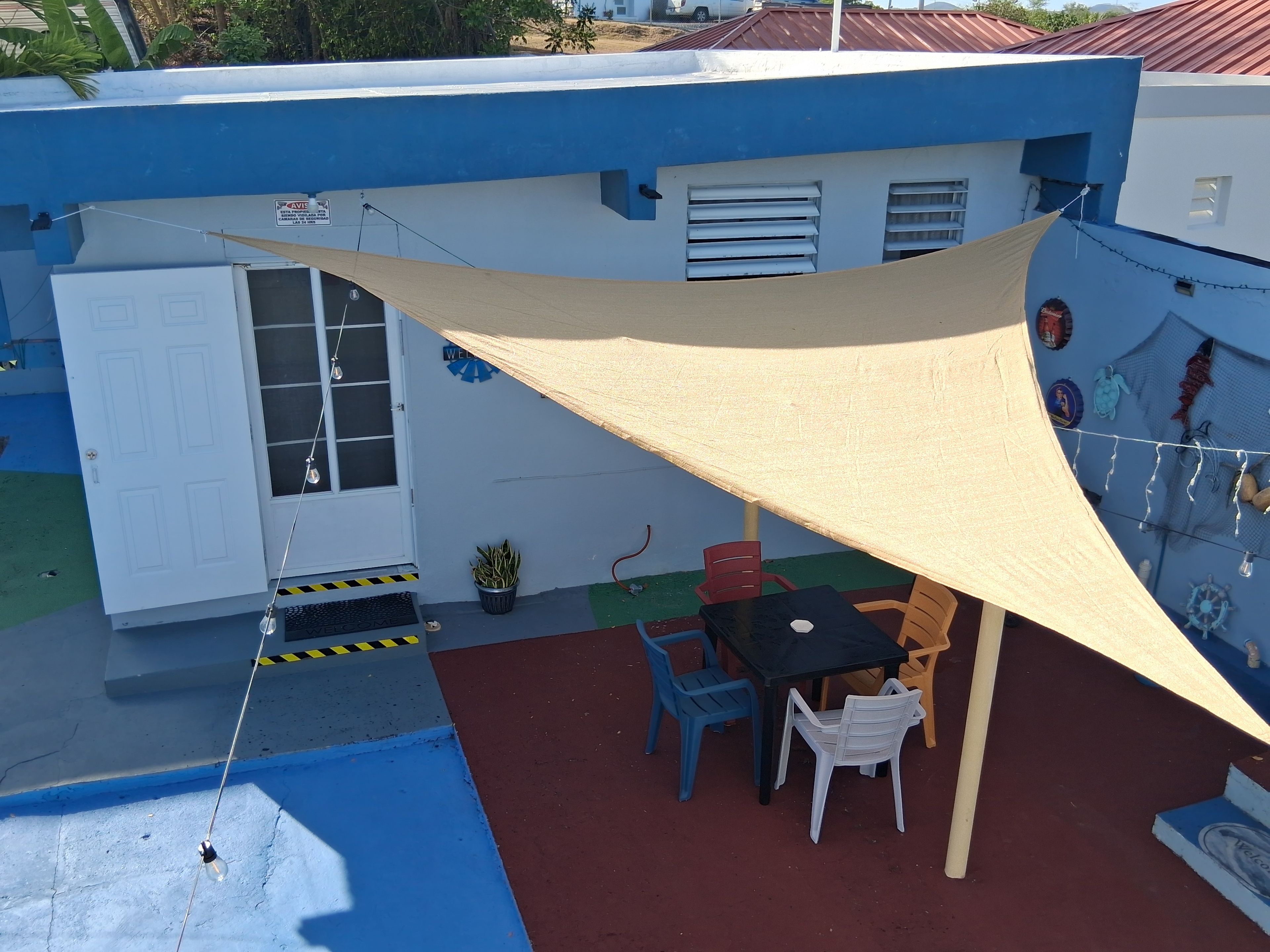 Un edificio azul con una puerta blanca, una mesa con sillas y una lámpara colgante.