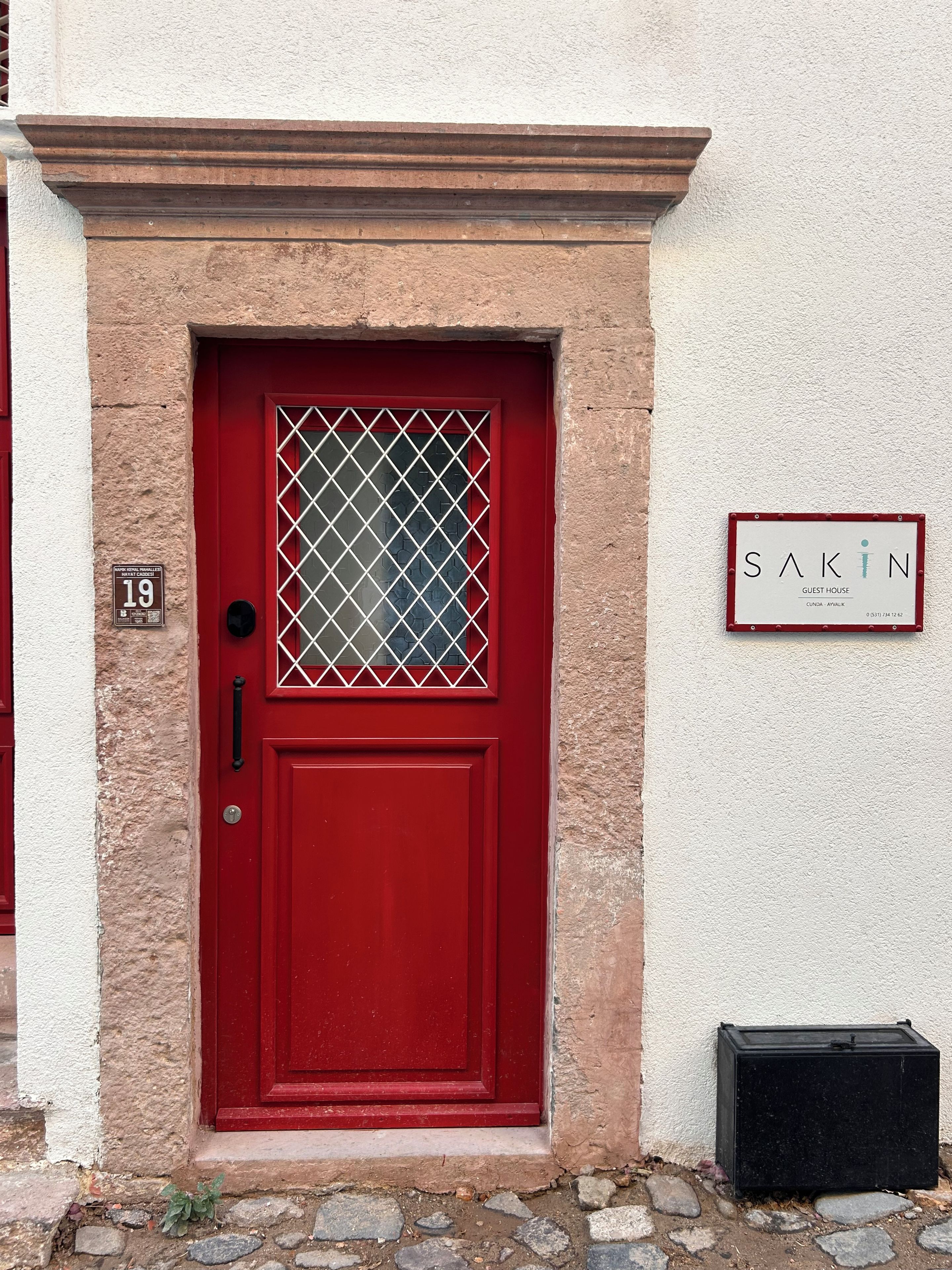 A red door with a glass panel and a sign indicating 'SAKIN GUEST HOUSE' with a phone number.