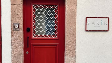 A red door with a glass panel and a sign indicating 'SAKIN GUEST HOUSE' with a phone number.