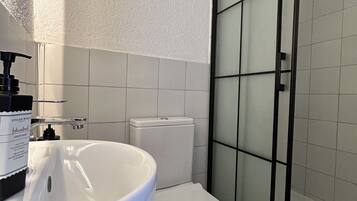 Ein Badezimmer mit weißem Waschbecken, einer Toilette und einer Duschkabine.