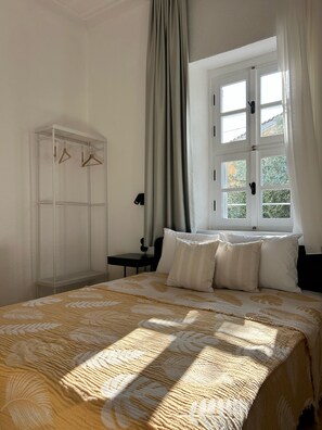 Un dormitorio con cama, armario, ventana y mesita de noche.