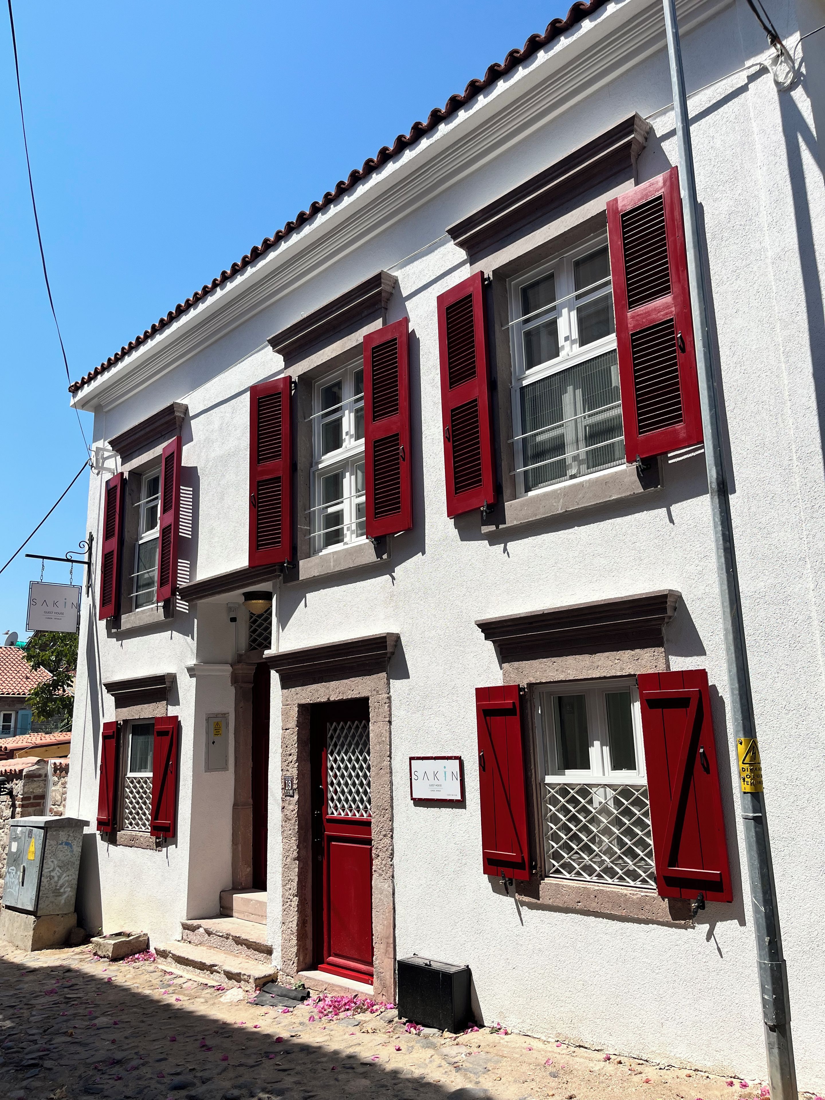 A building with multiple windows, red shutters, and a sign indicating it is a guest house.