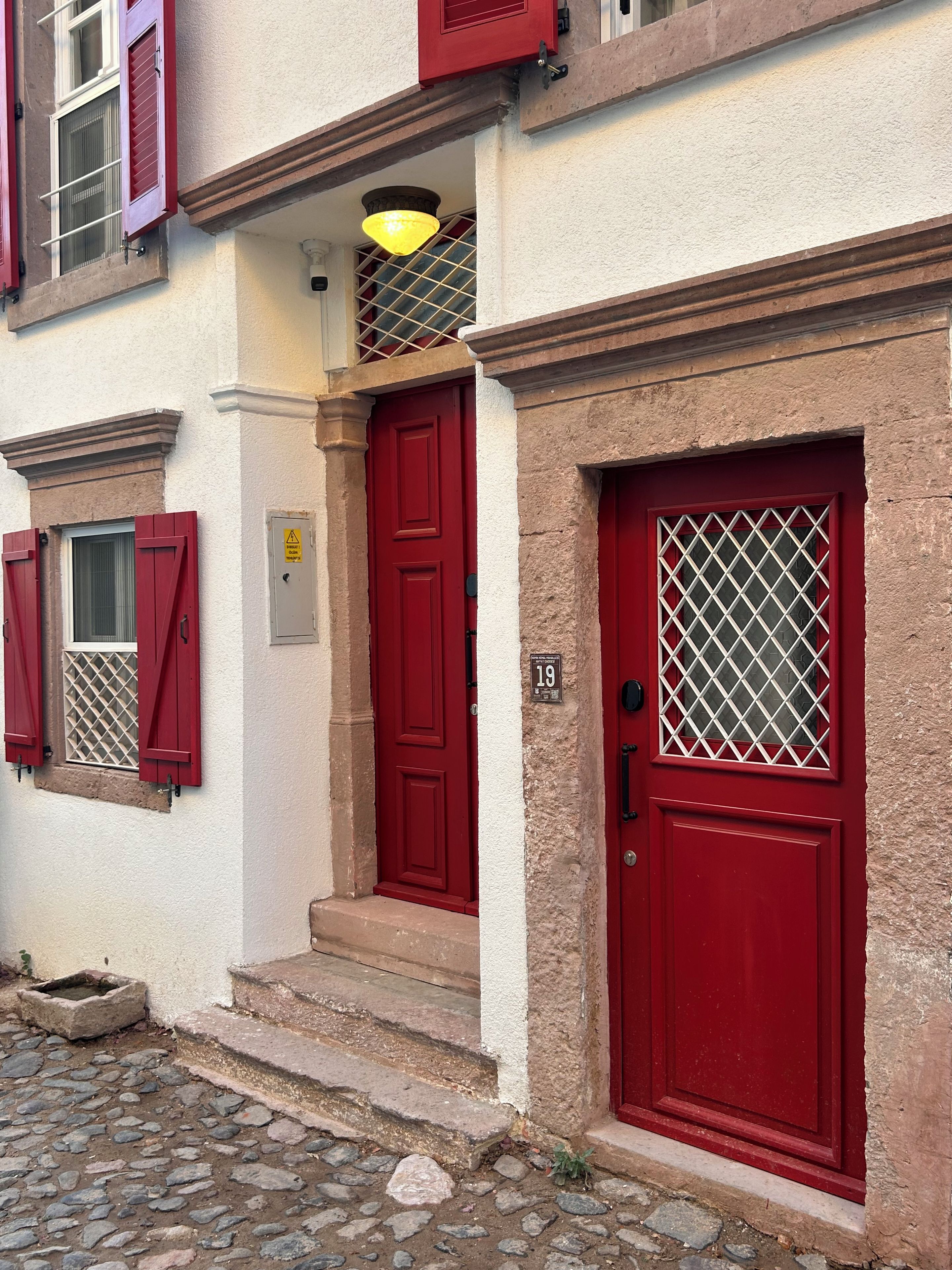 Um edifício com portas e janelas vermelhas, entrada com piso de pedra e luminária amarela sobre a porta.