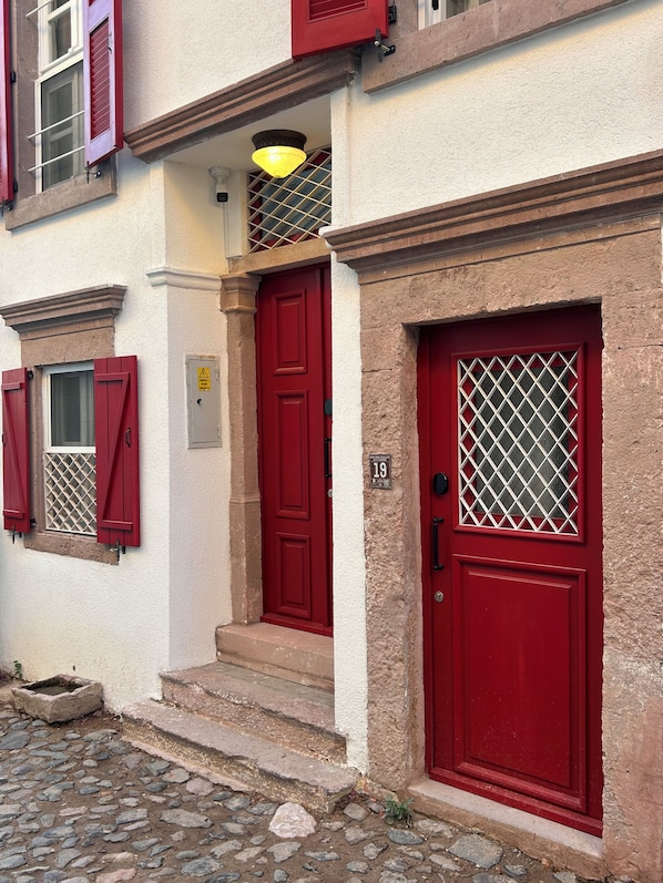 A building with red doors and windows, a stone-paved entrance, and a yellow light fixture above the door.