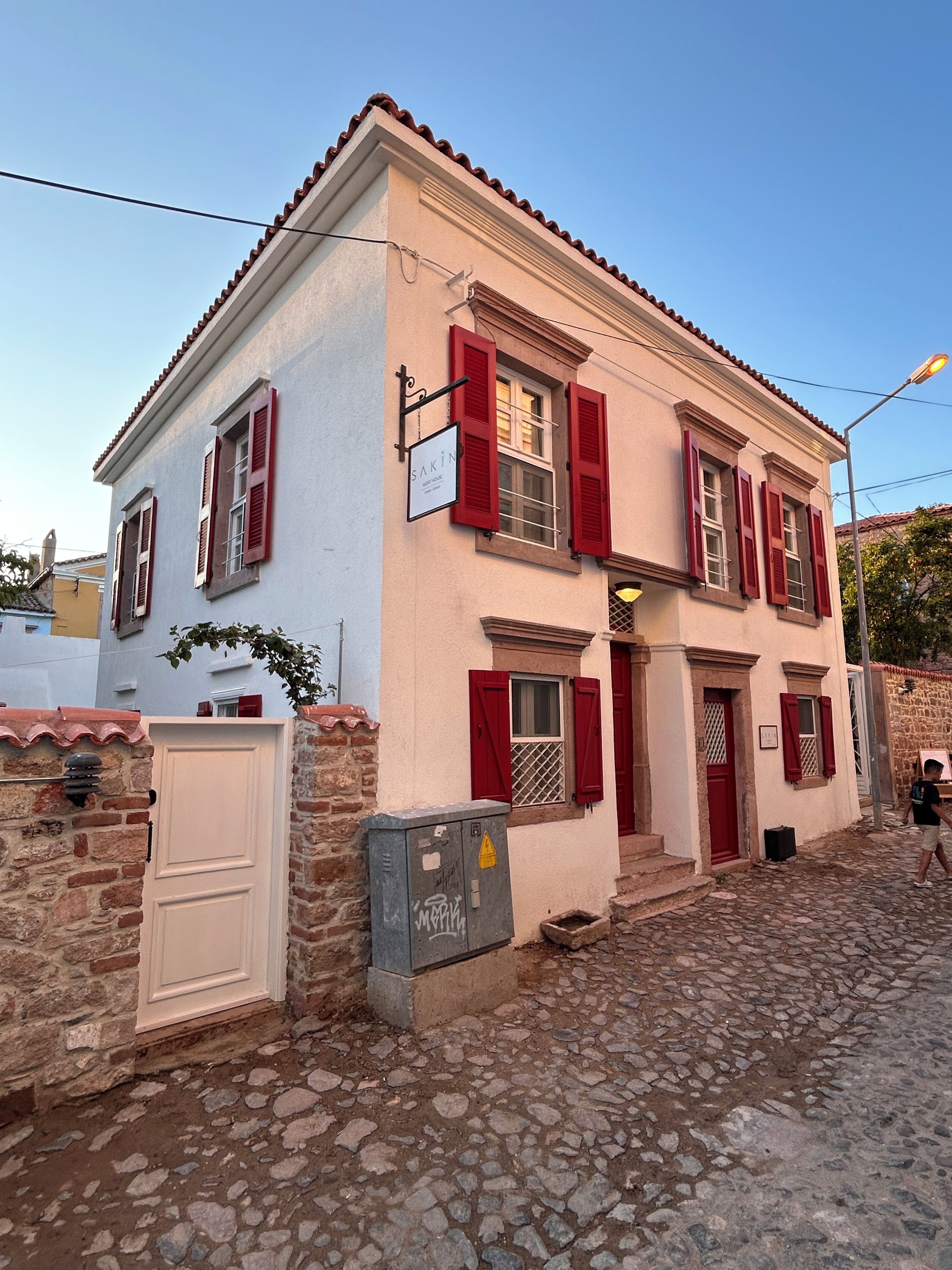 A two-story building with red shutters, a white door, and a stone wall.