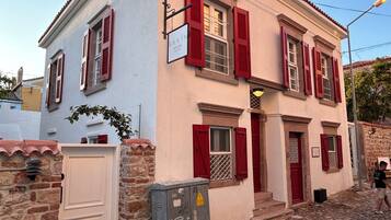 A two-story building with red shutters, a white door, and a stone wall.