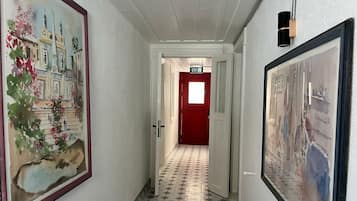 A hallway with a tiled floor, a red door, and framed artwork on the walls.