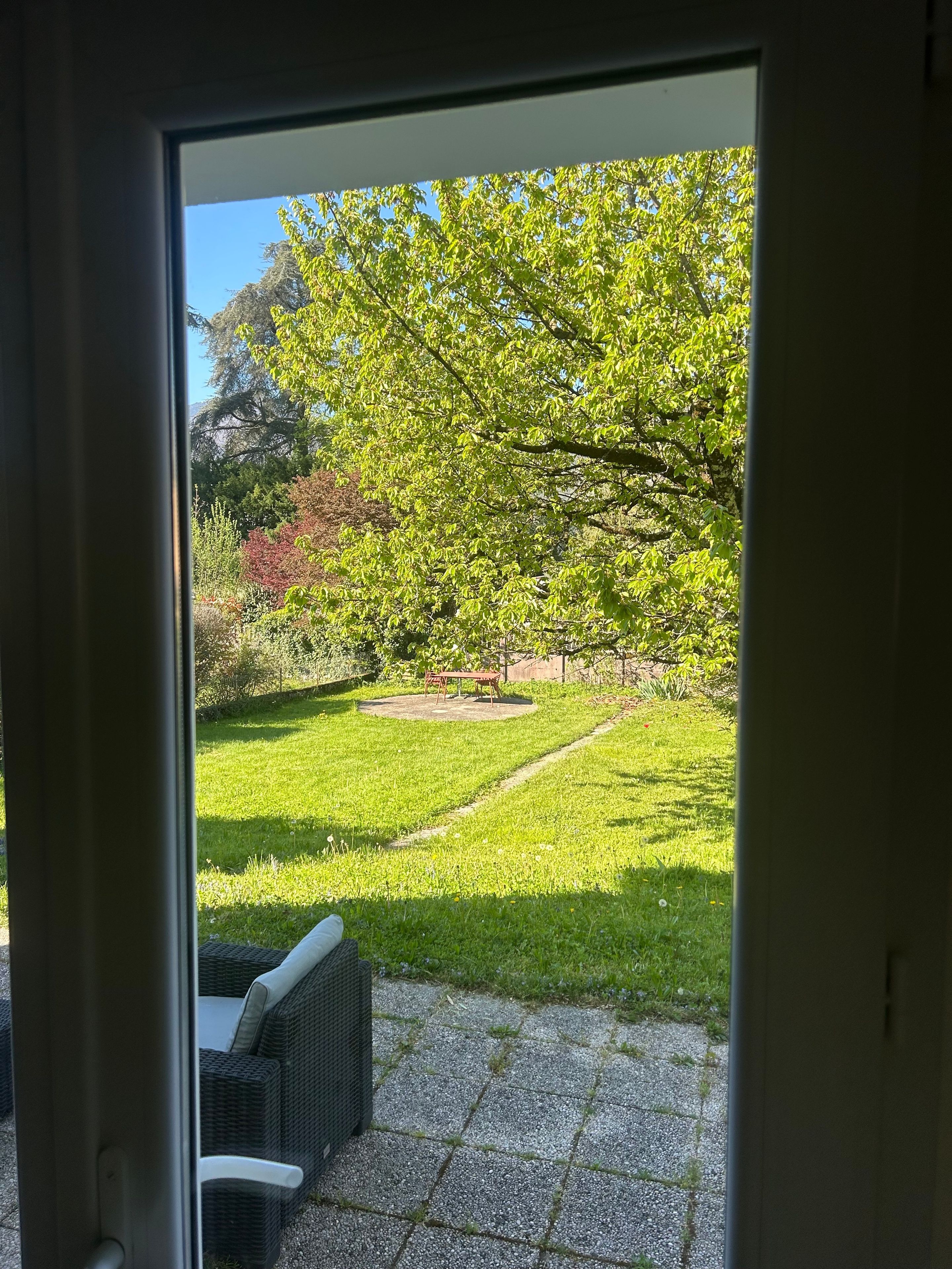 Vista attraverso una porta vetrata su un patio con prato, altalena e sedia in vimini.