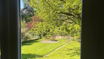 Vista attraverso una porta vetrata su un patio con prato, altalena e sedia in vimini.
