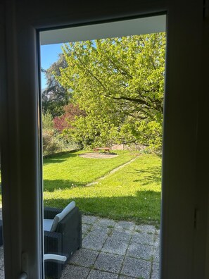Blick durch eine Glastür auf einen Patio mit Rasen, einer Schaukel und einem Korbstuhl.