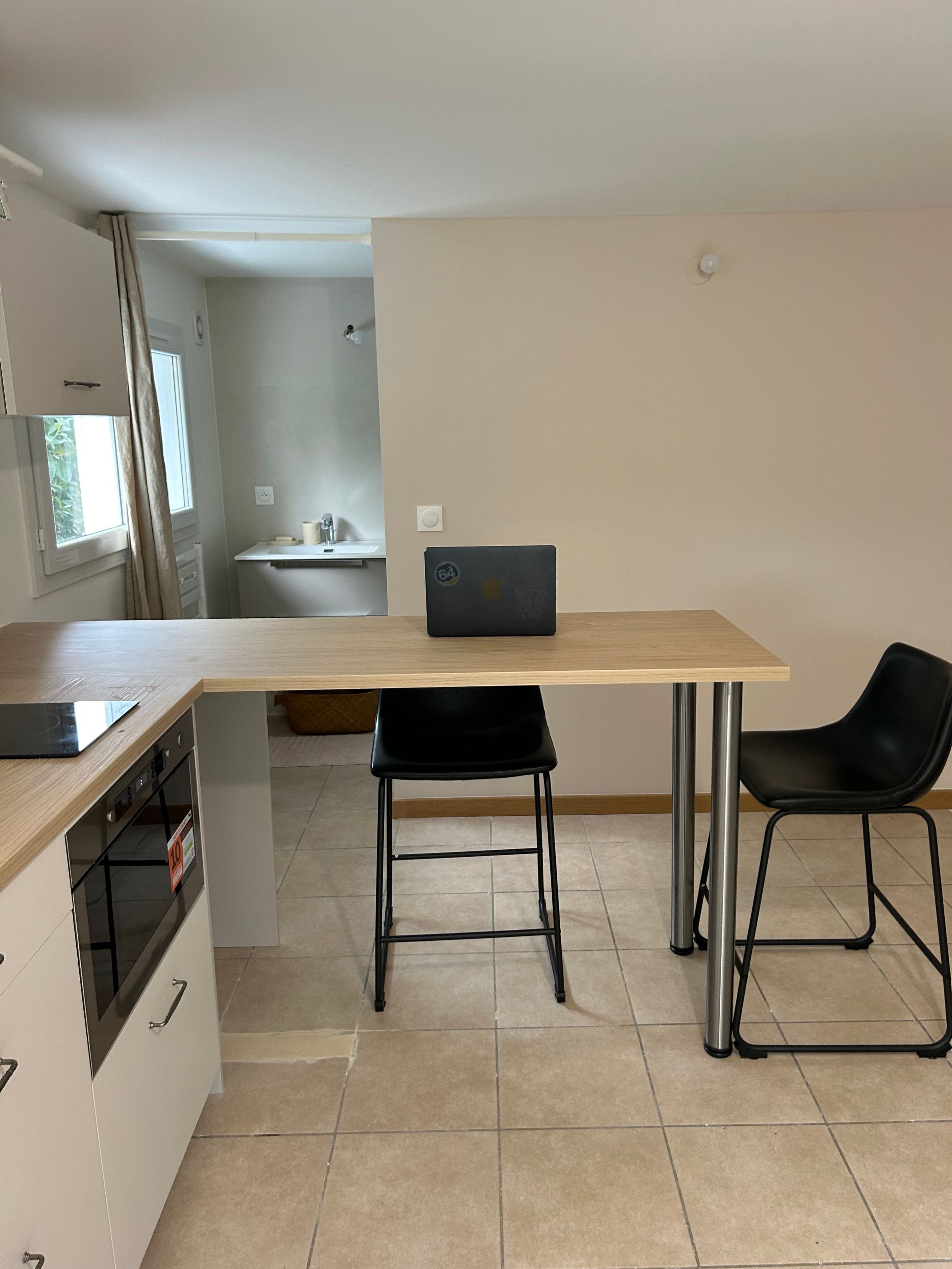 A compact kitchen with a dining area, a laptop on the table, and a black chair.