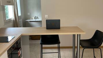 A compact kitchen with a dining area, a laptop on the table, and a black chair.