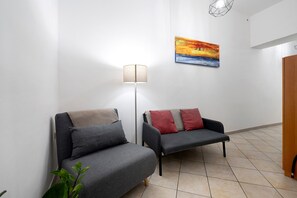 Un couloir avec deux canapés gris, un lampadaire, un tableau et une porte en bois.